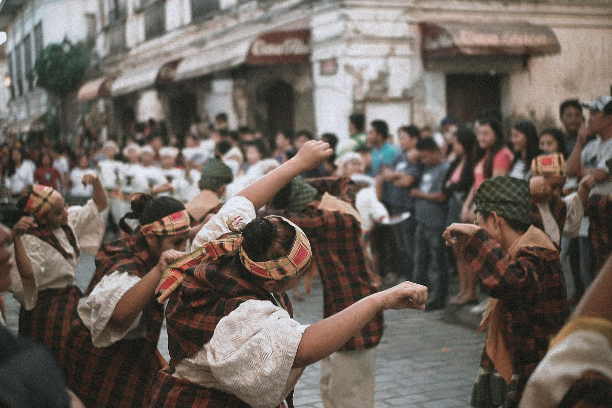 A group of performers in traditional clothing dances in a street while a crowd watches. A group of performers in traditional clothing dances in a street while a crowd watches.