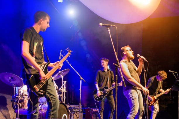 A band performs on stage with various instruments and vibrant lighting. A band performs on stage with various instruments and vibrant lighting.