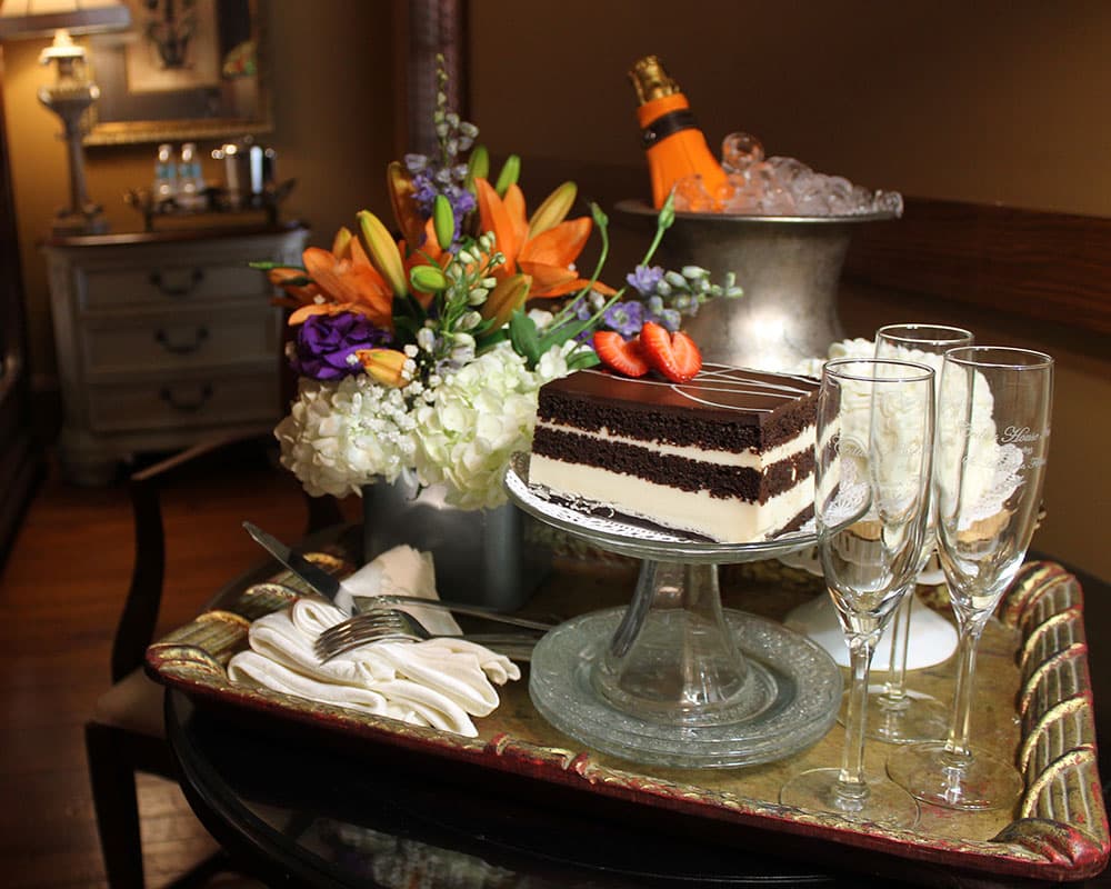 A chocolate cake with strawberries, champagne in a bucket, and elegant glasses on a decorative tray.