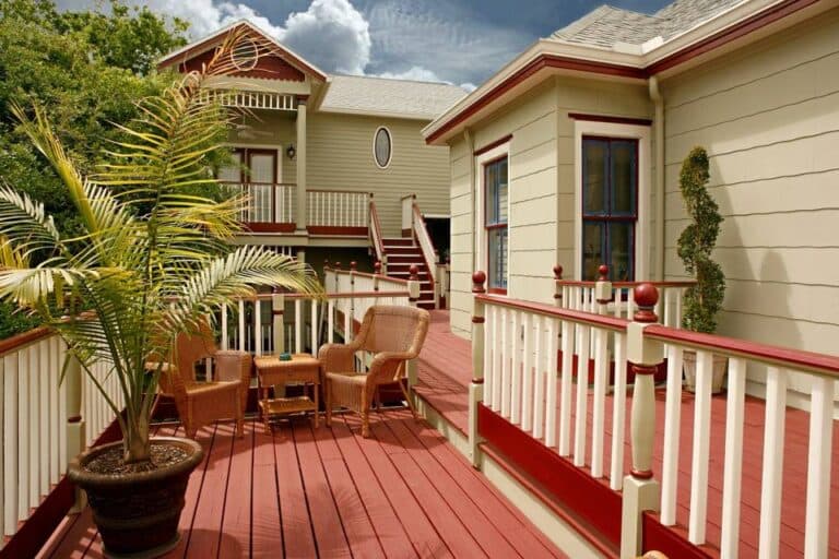 A sunny deck with wooden railings, two chairs, and tropical plants beside cozy homes. A sunny deck with wooden railings, two chairs, and tropical plants beside cozy homes.