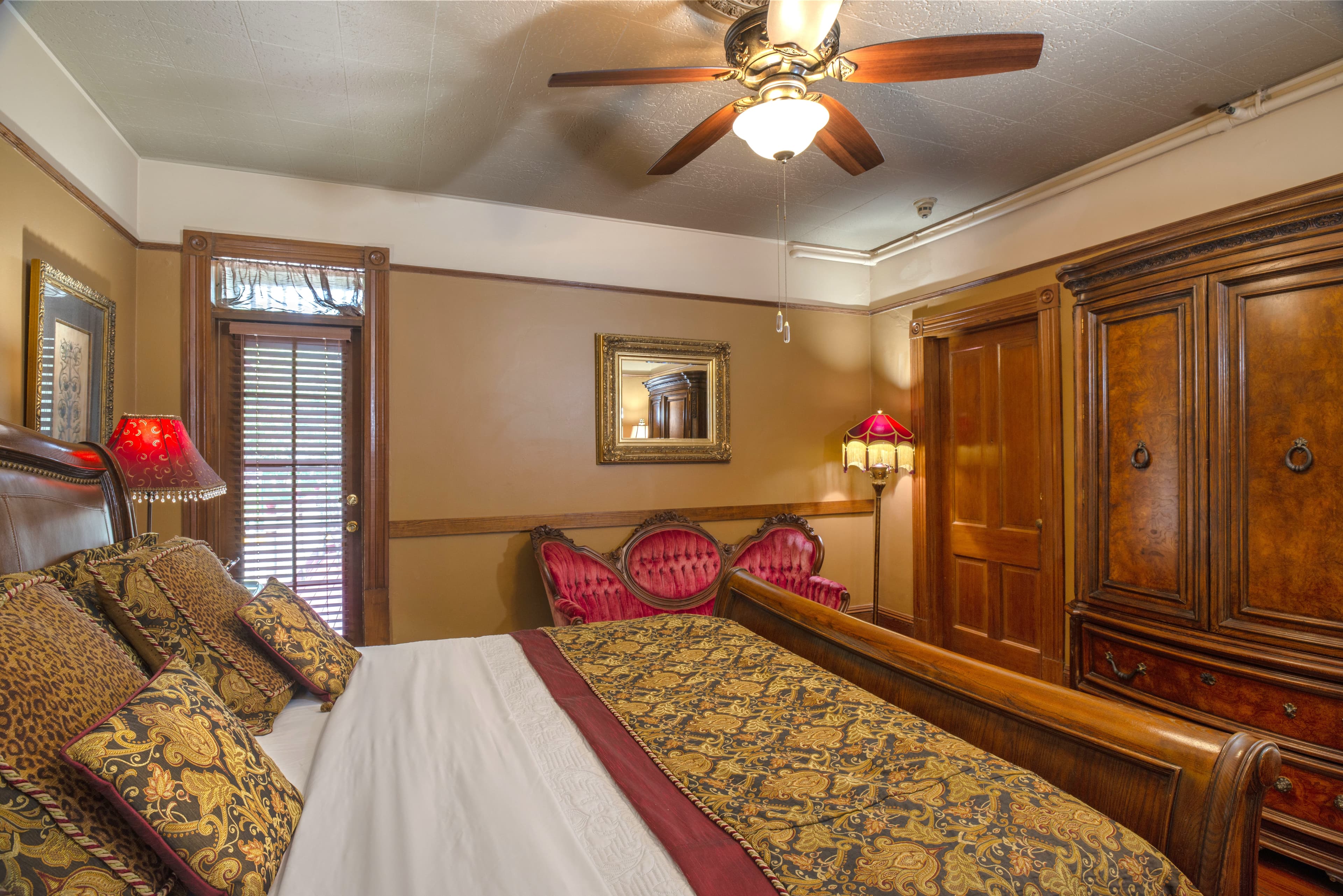 A luxurious room with a large bed, a dark wood dresser, a red couch, and a sitting area with a lamp. A framed picture hangs on the wall above the bed.