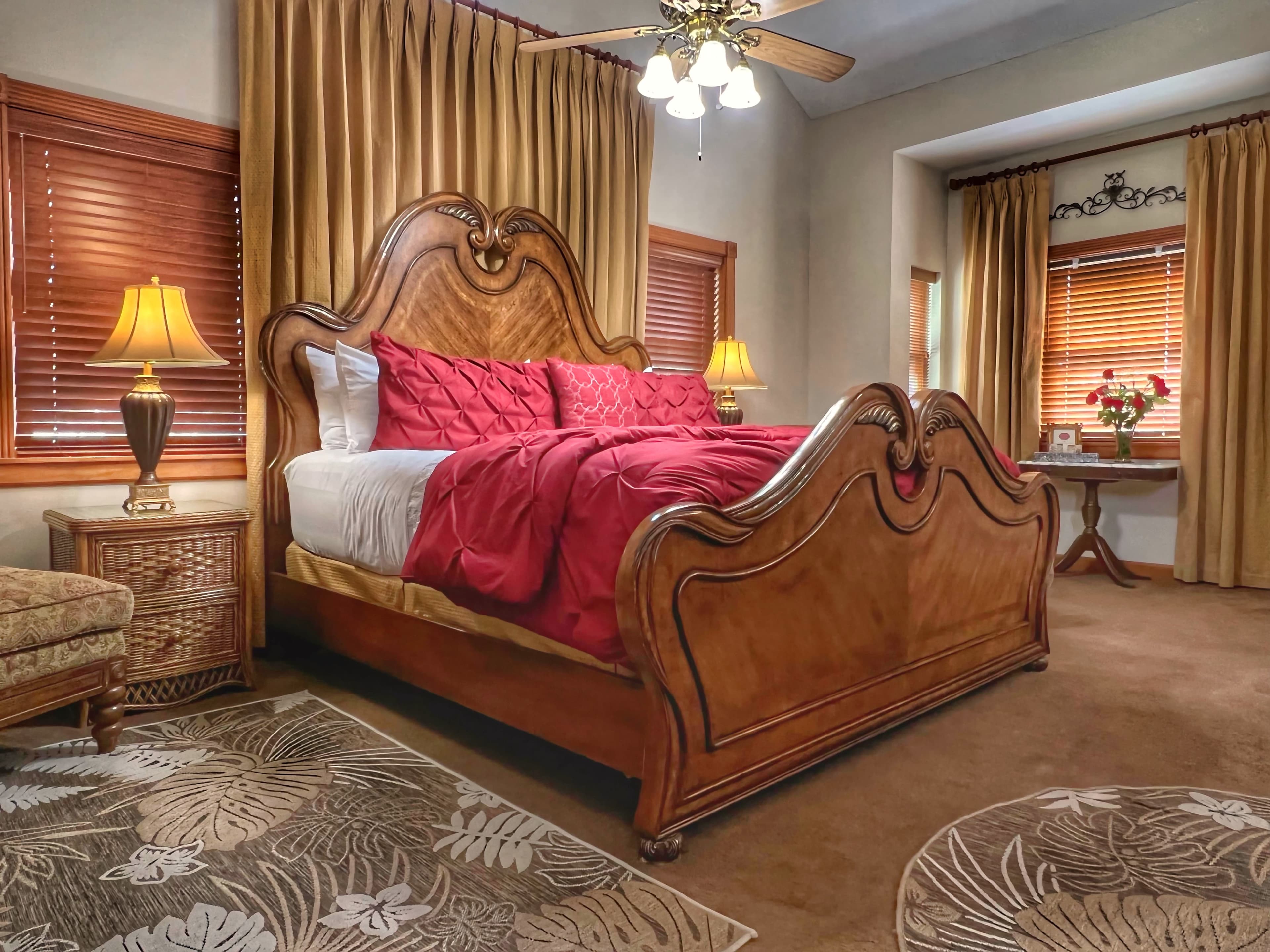 A stately room with a gorgeous wooden bed, a dresser, a sitting area with a chair and a lamp, and a window with curtains.