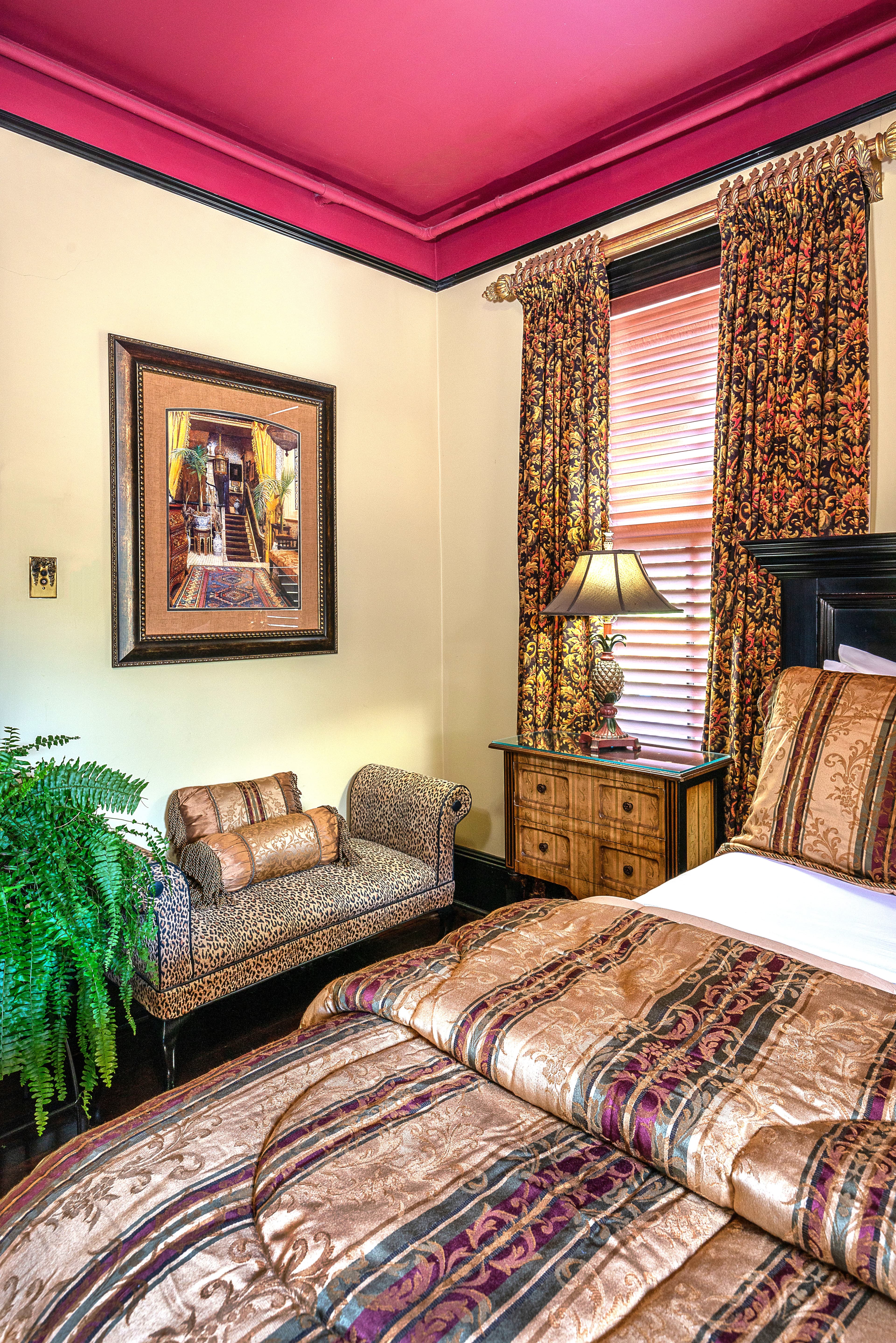 A beautifully decorated bedroom featuring a patterned bedspread, a vintage lamp, and elegant curtains.