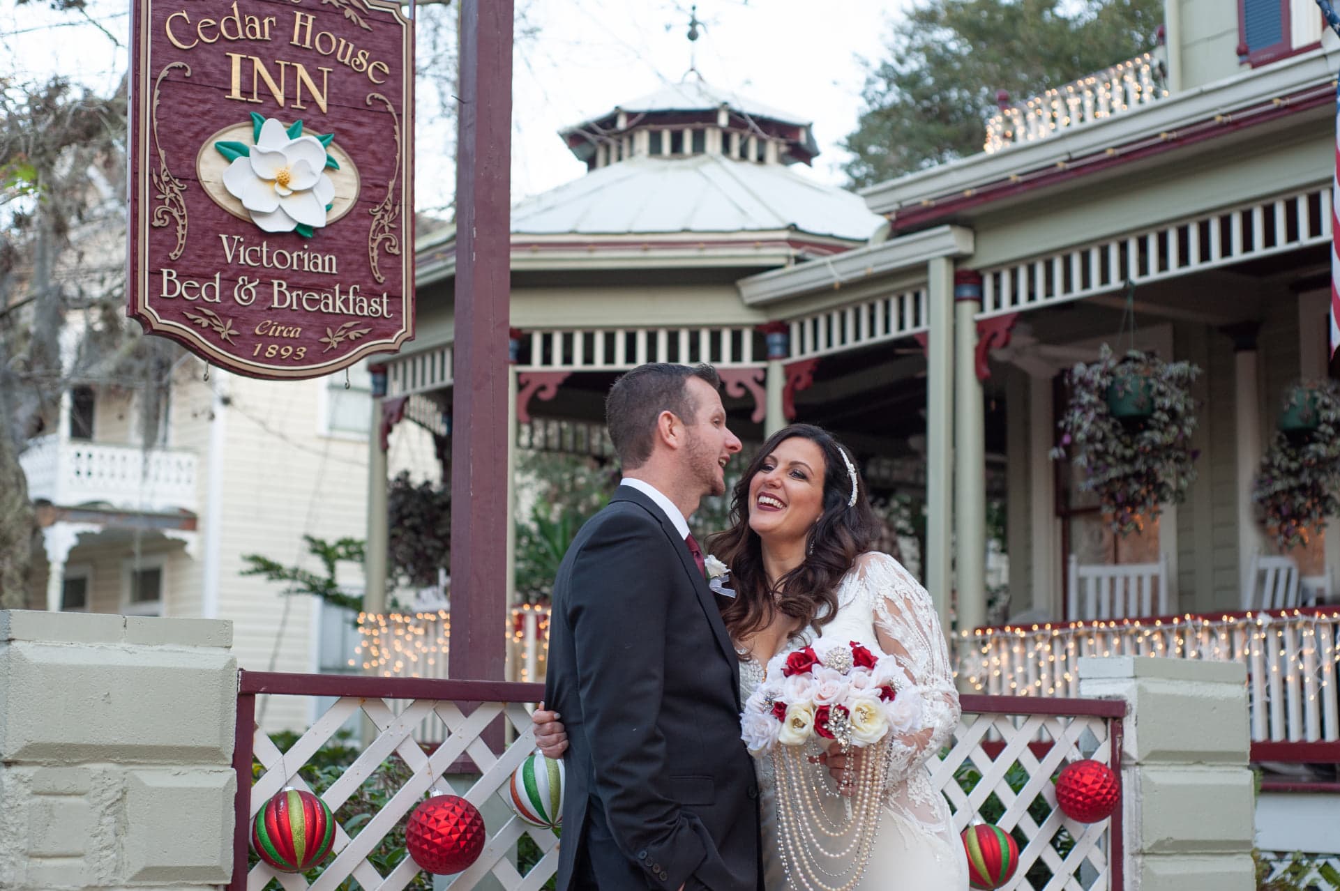 A couple joyfully embraces in front of a Victorian bed and breakfast, holding a bouquet of flowers. A couple joyfully embraces in front of a Victorian bed and breakfast, holding a bouquet of flowers.