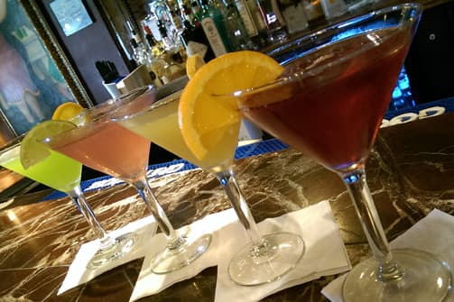 A row of colorful cocktails, garnished with fruit slices, on a bar counter.