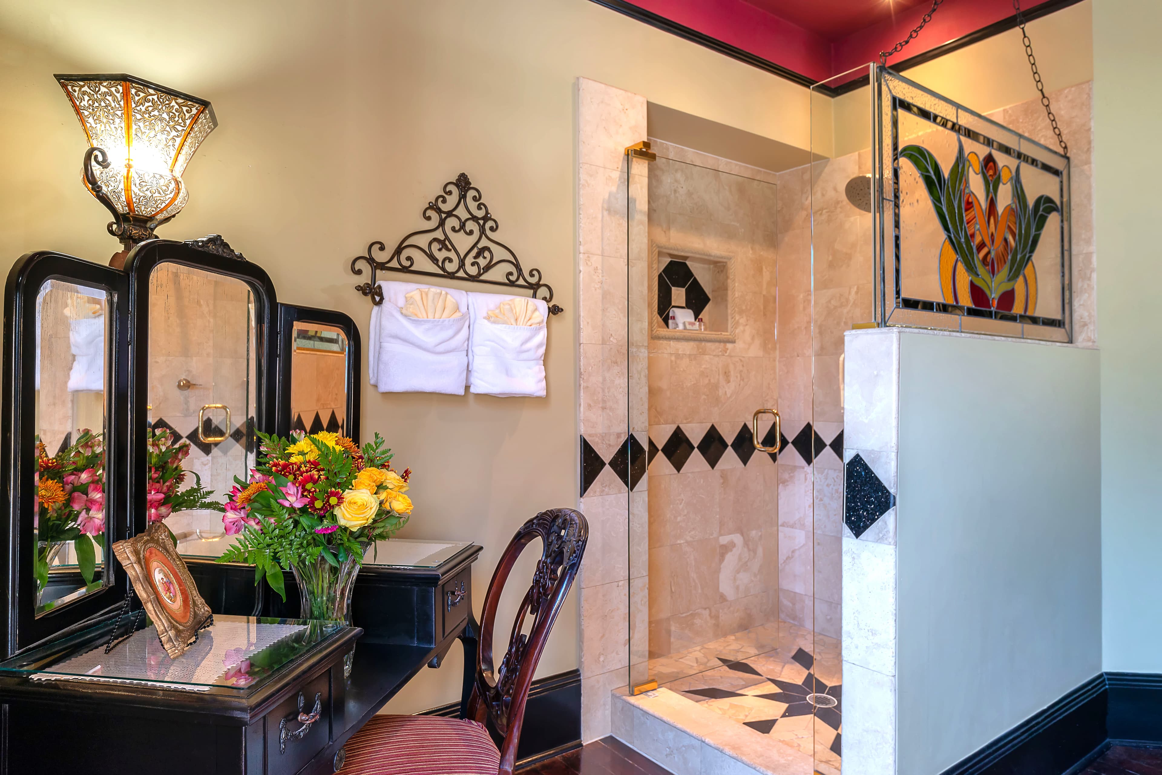 A stylish bathroom featuring a shower area, antique vanity, and floral arrangement.
