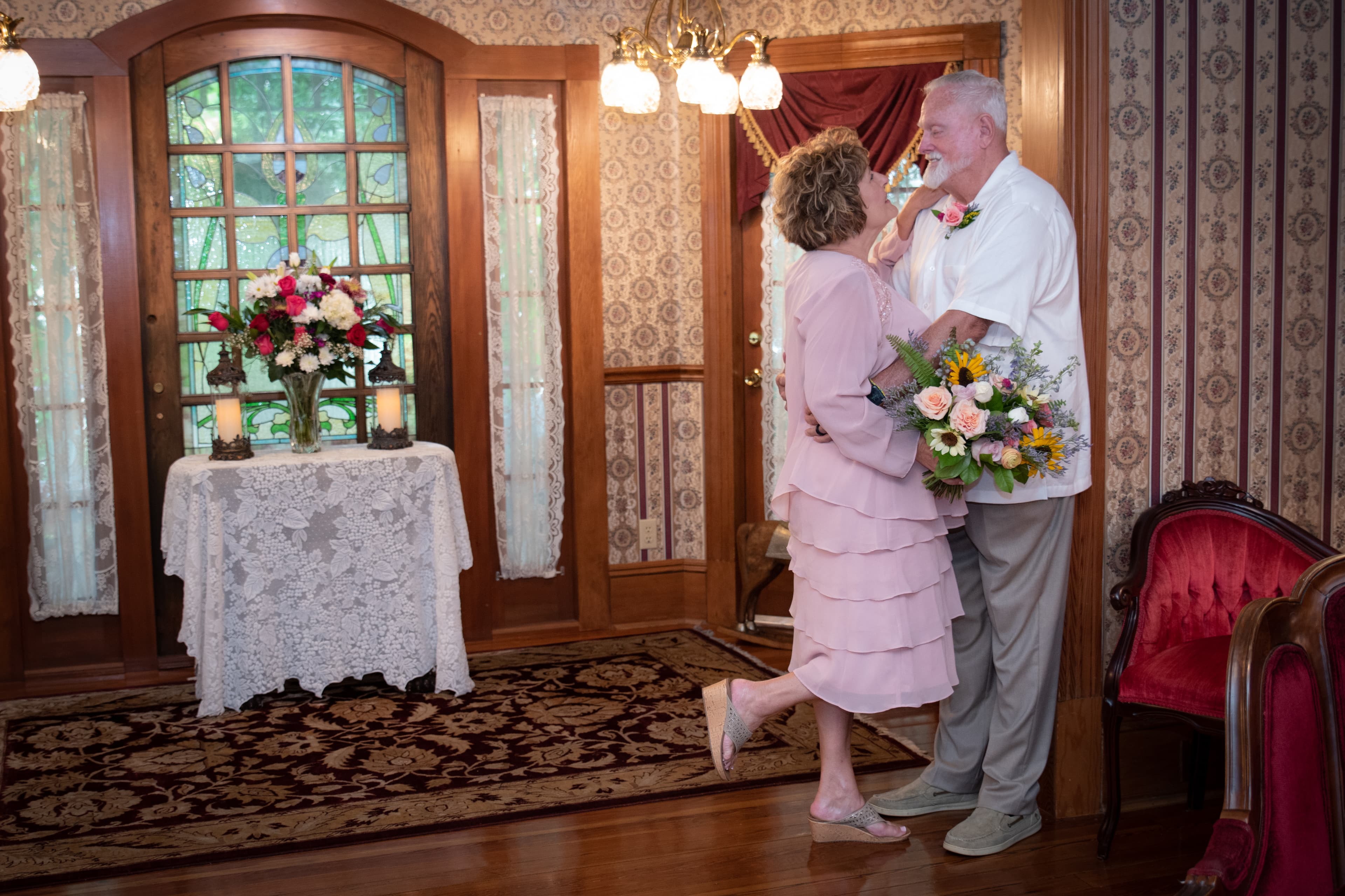 A couple joyfully embraces in a beautifully decorated room with a bouquet and floral arrangement.