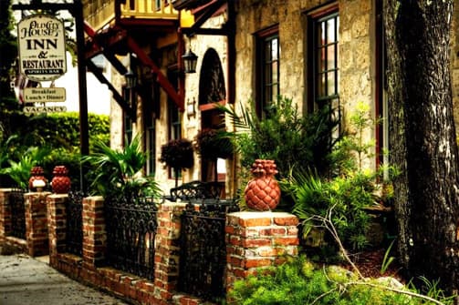 A quaint inn's exterior features brick walkways, lush greenery, and decorative pineapple accents.