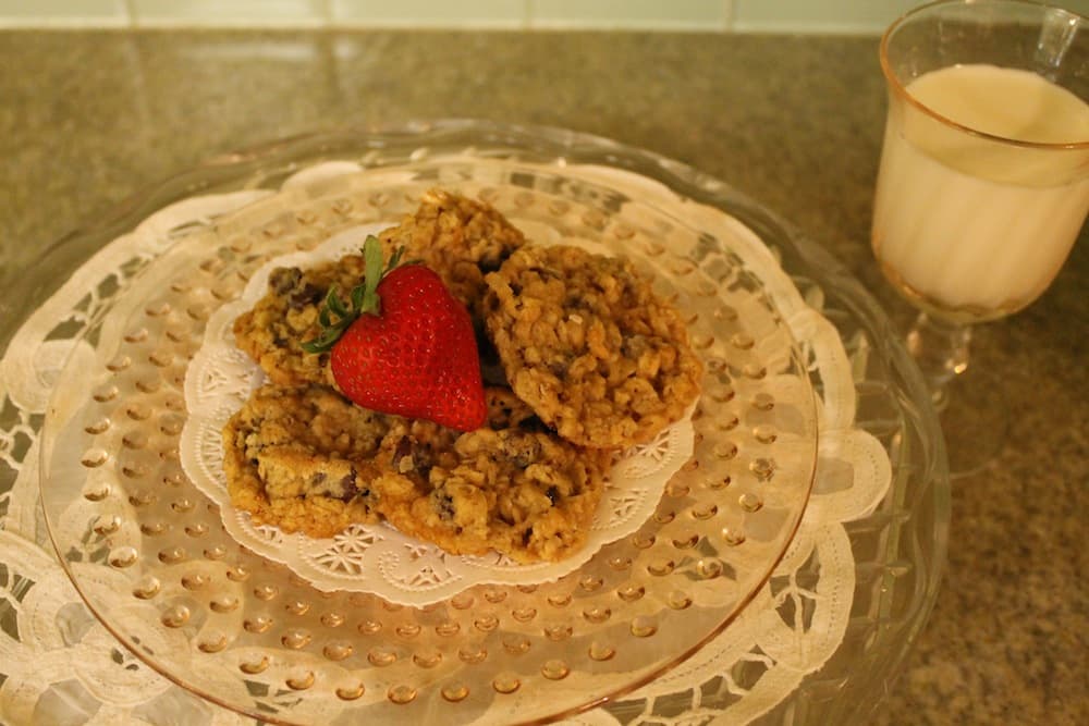 A plate of oatmeal cookies topped with a fresh strawberry next to a glass of milk. A plate of oatmeal cookies topped with a fresh strawberry next to a glass of milk.