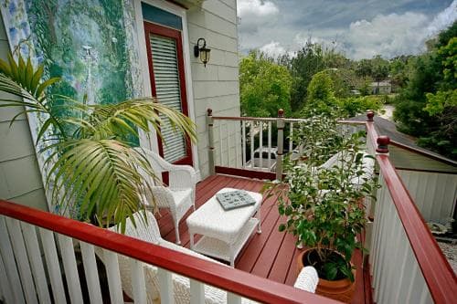 A cozy balcony with white chairs, potted plants, and a scenic view under a cloudy sky. A cozy balcony with white chairs, potted plants, and a scenic view under a cloudy sky.