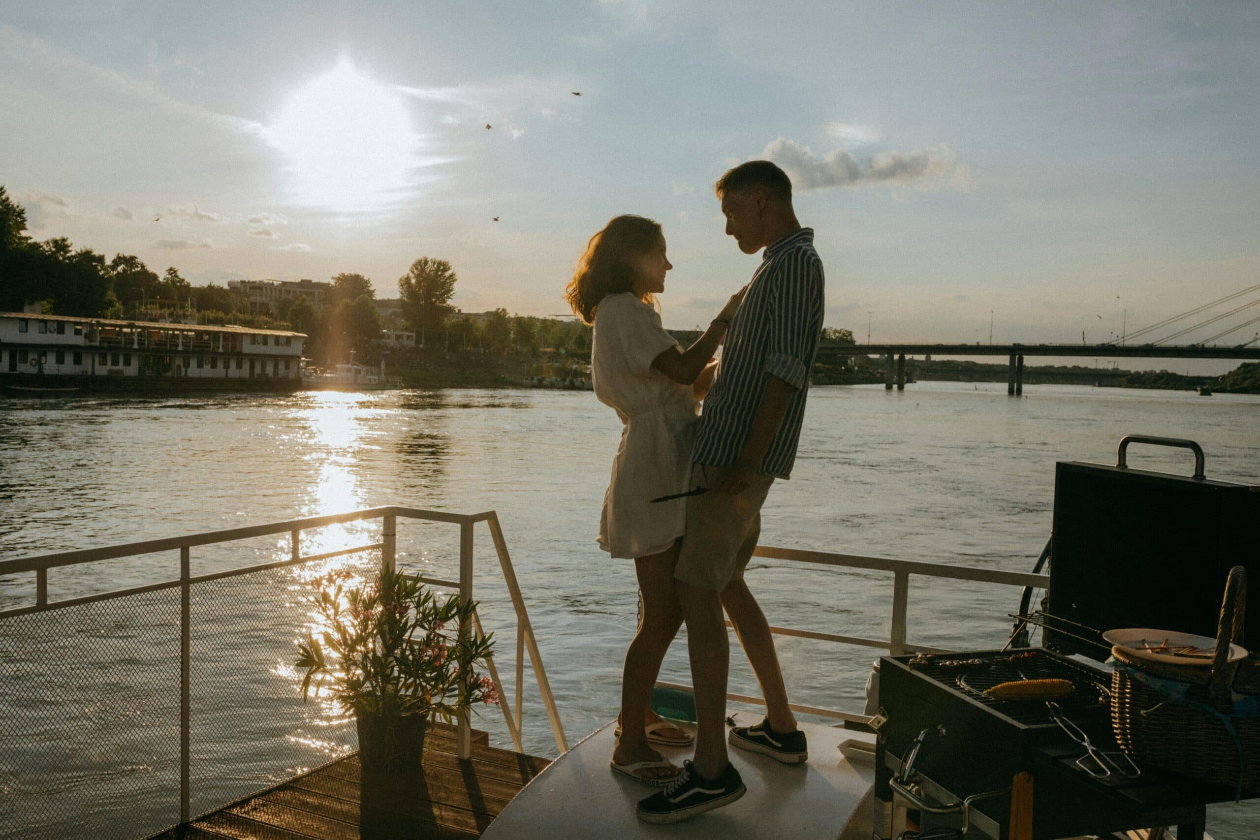 A couple stands on a boat at sunset, enjoying a romantic moment by the water.