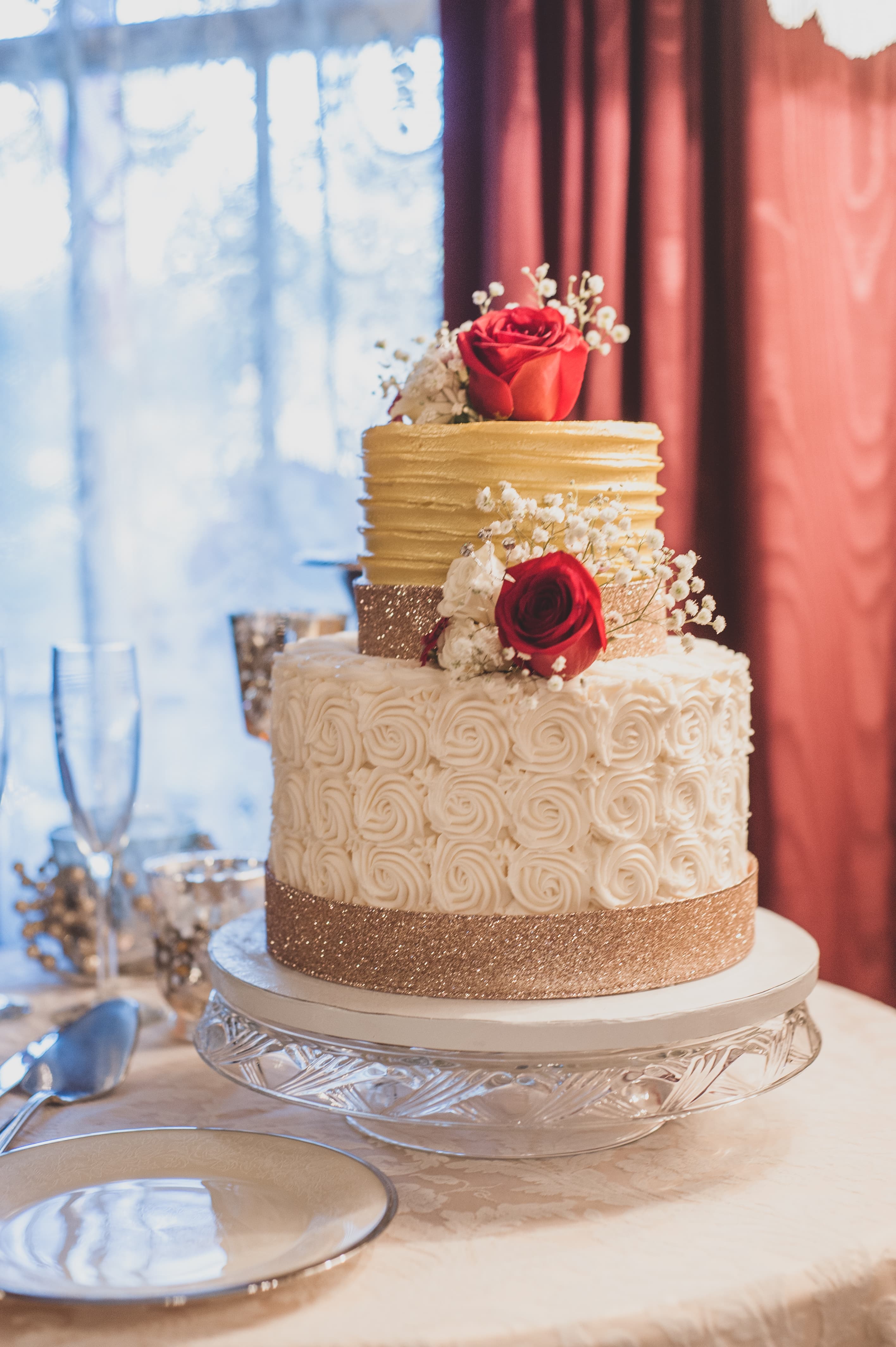 A two-tiered wedding cake decorated with gold and white icing, rose flowers, and a glittery band.
