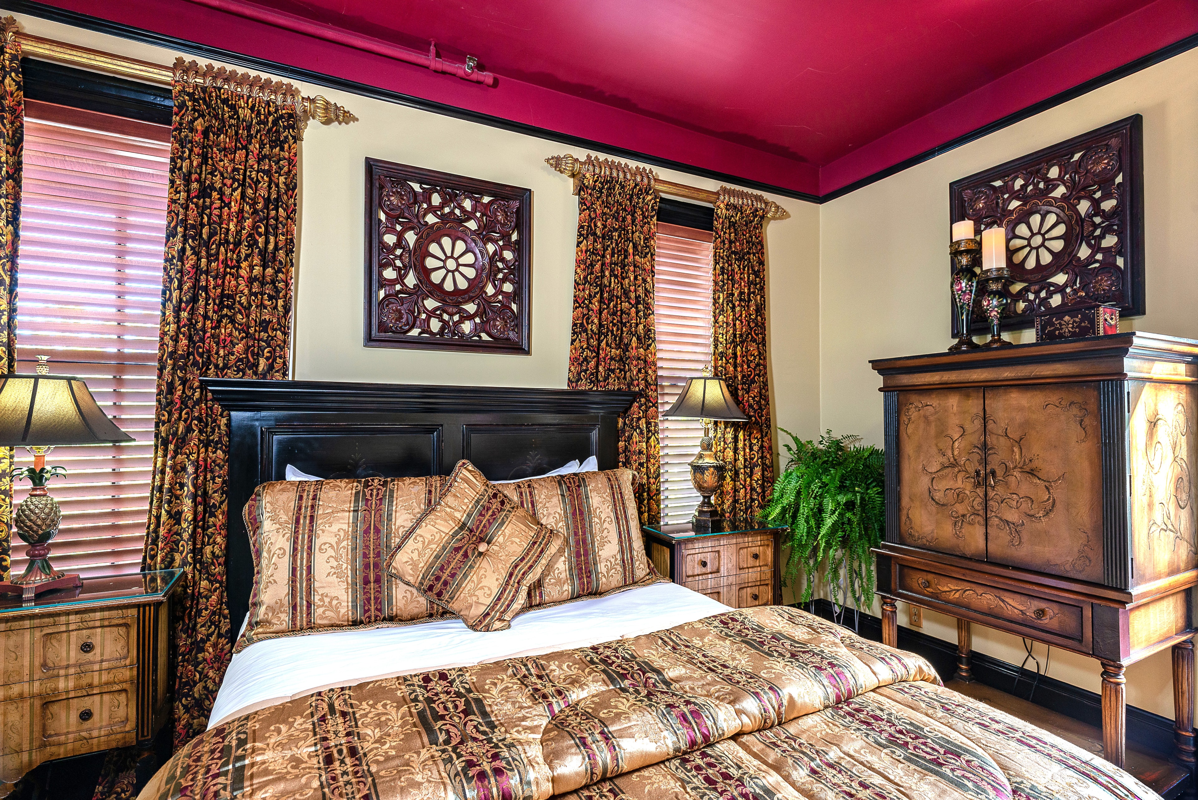A cozy bedroom featuring a black wooden bed with ornate bedding, decorative curtains, and vintage furniture against a vibrant pink ceiling.